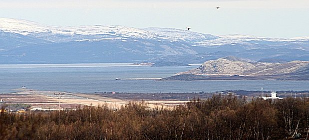 Utsikt over Porsangerfjorden med flyplassen i forgrunnen, og to F5 jagerfly i luften.